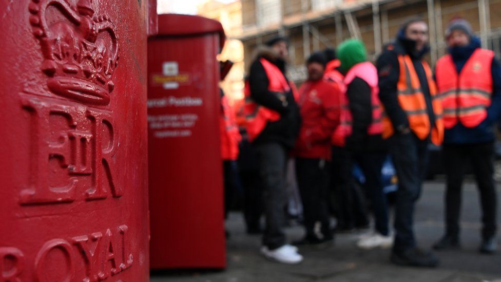 Striking Royal Mail workers stand behind post box