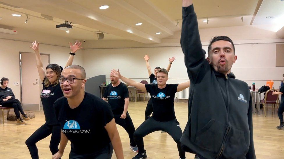 Several men in black t-shirts and shorts dancing
