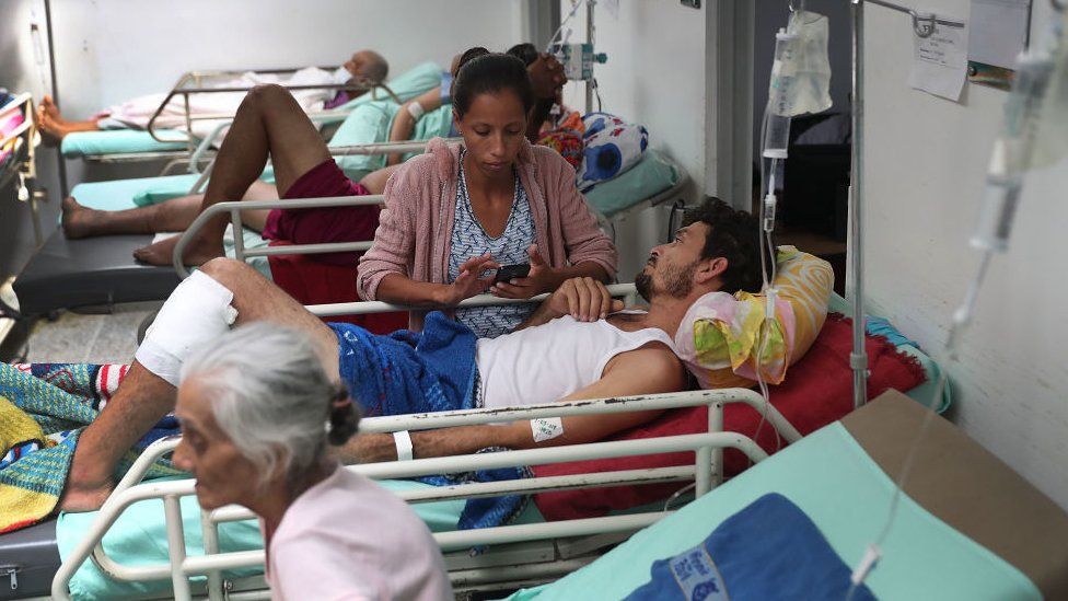 Veronica Calmenarez stands with her husband Luis Alfredo Lopez Molina, (C) both of whom are originally from Venezuela, as he receives health care in the emergency room of the University Hospital Erasmo Meoz after seeking medical care for a severe infection on his leg on March 1, 2019 in Cucuta, Colombia.