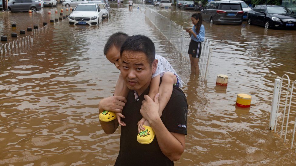 Man carries child while walking through Beijing street flooded by super typhoon Doksuri