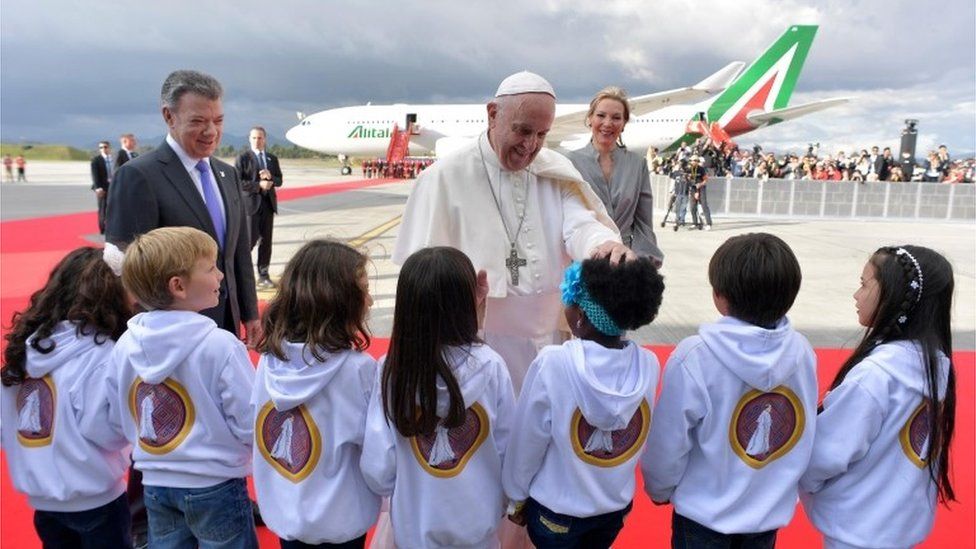 Colombian President Juan Manuel Santos (L) and his wife Maria Clemencia Rodríguez (R) look on as Pope Francis (C) greets children after disembarking from an aircraft upon his arrival at Bogotá on 6 September 2017.