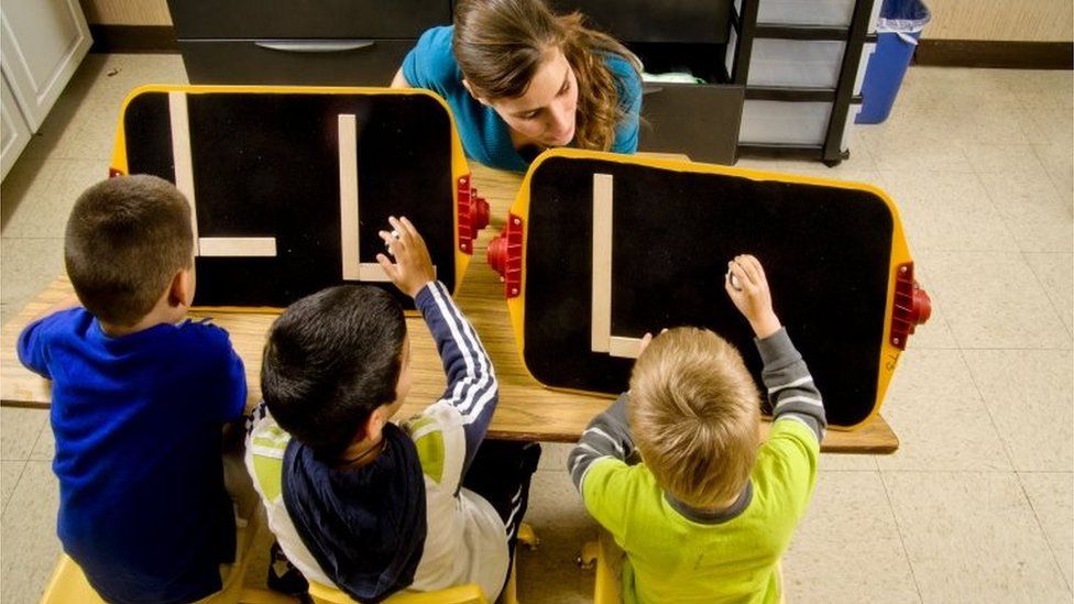 Teacher helps boys make alphabet letters