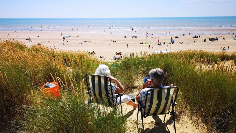 A man and woman relax on deckchairs in the sand dunes at Camber Sands