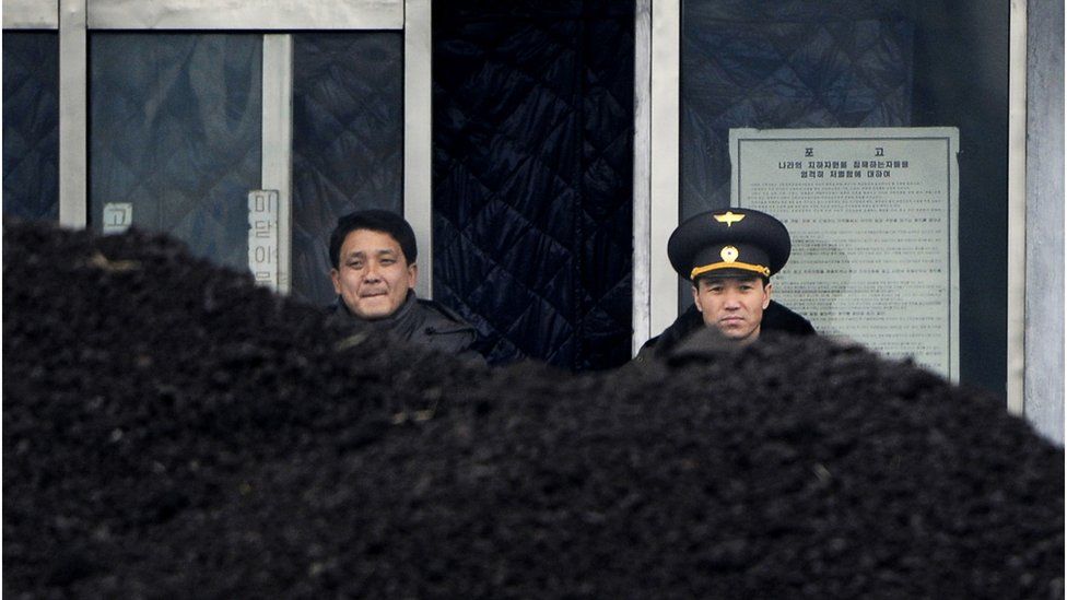 A North Korean military officer and a North Korean man standing behind a pile of coal along the banks of the Yalu River in the North Korean border town of Siniuju.
