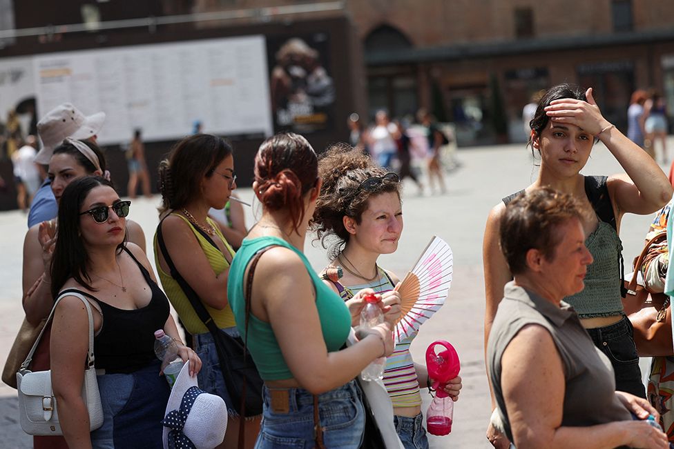 Люди стоят в очереди, чтобы наполнить свои бутылки с водой у фонтана Нептуна в Болонье, Италия, 18 июля 2023 года
