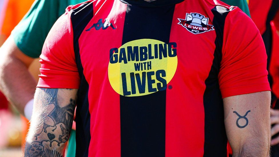 Close up image of a footballer in a red and black striped Lewes FC football shirt with a logo on the front.