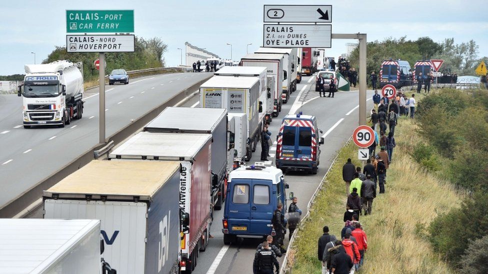 Lorries queuing for the port at Calais in August and watched by migrants