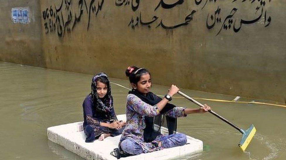 Girls use a temporary raft across a flooded street in a residential area after heavy monsoon rains in Karachi on July 26, 202