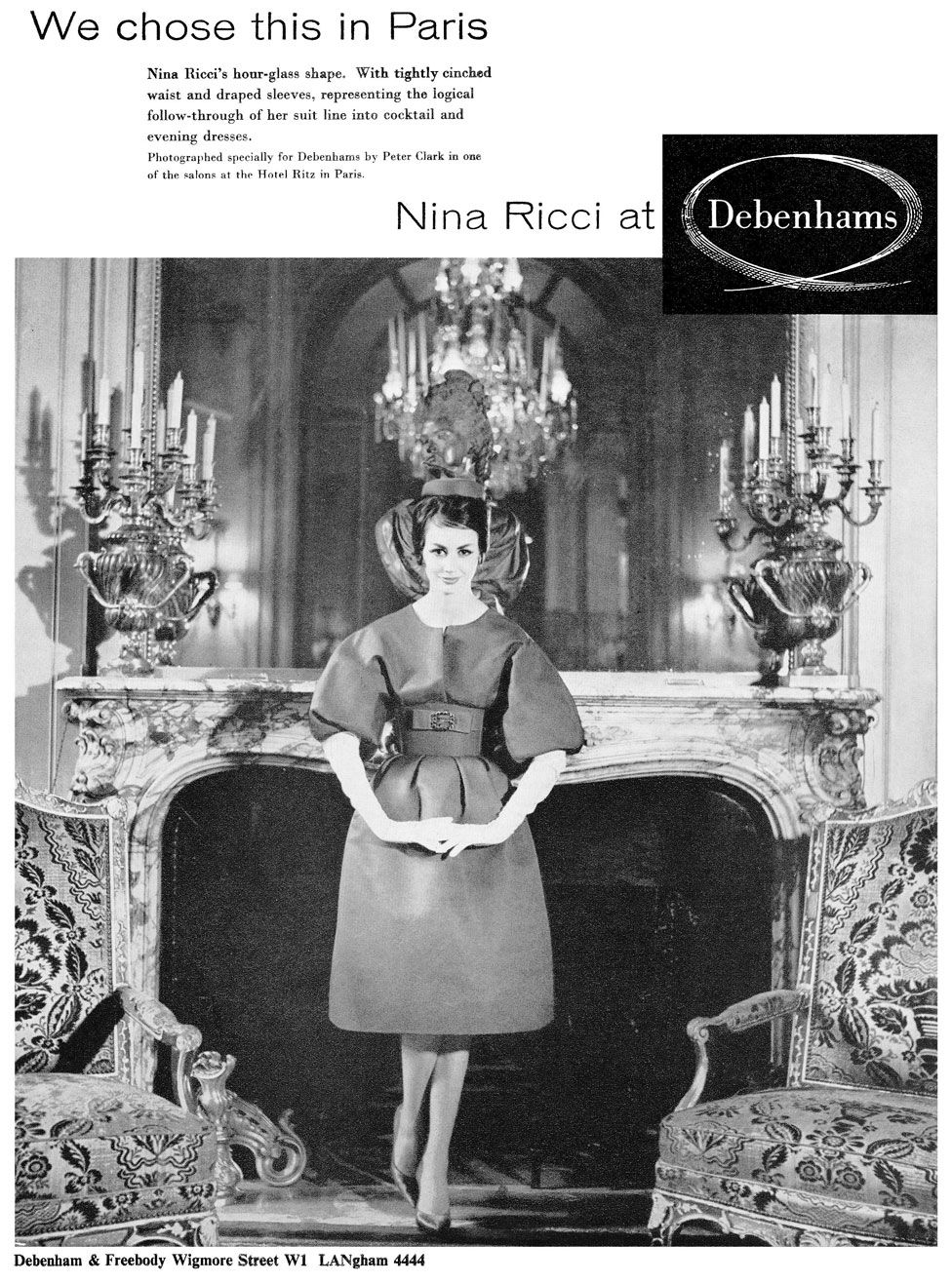 An advert for a fashion brand showing a woman in a dress standing in front of an elegant fireplace