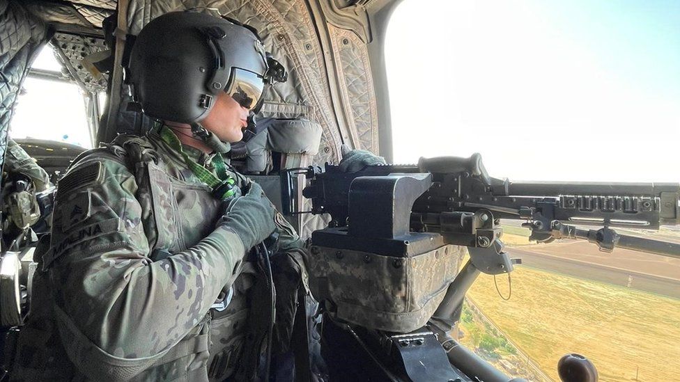 US service member holds a machine gun on board a helicopter