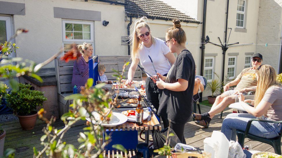 Family sitting on garden furniture, having a barbecue