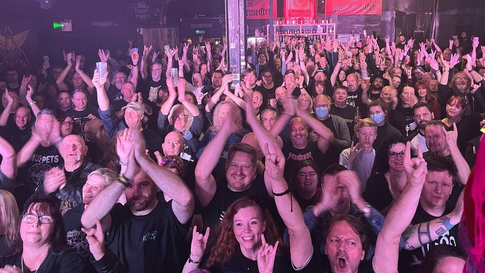 A crowd of people cheering in a music venue