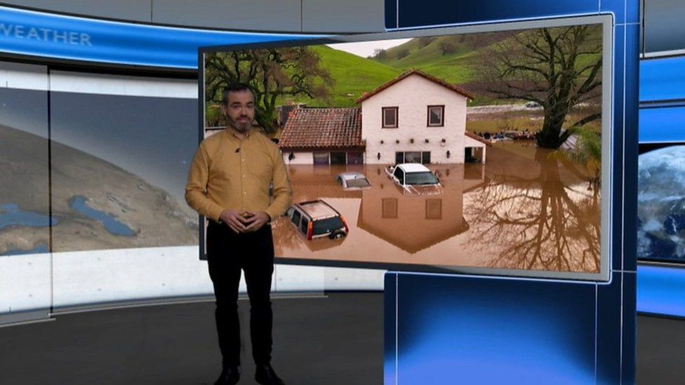 Ben Rich standing in front of an image of a house surrounded by flood water