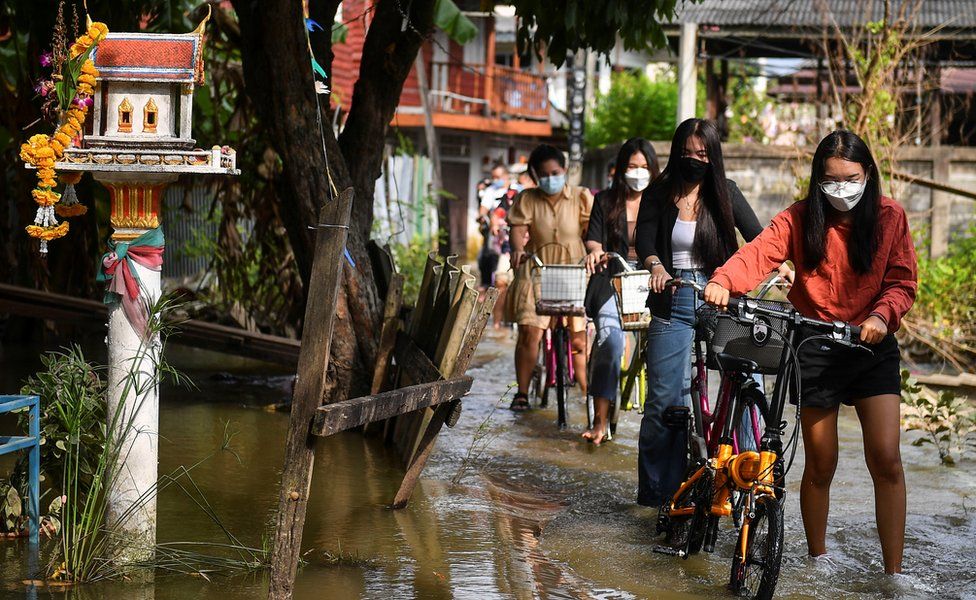 People wade through a flooded street with their bicycles in Nonthaburi province, on the outskirts of Bangkok