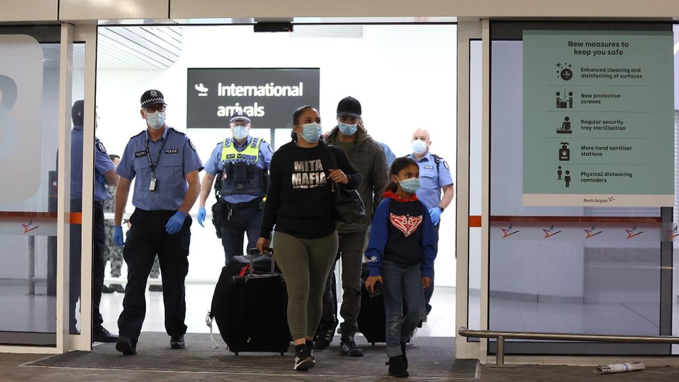 Police at Sydney Airport escort a family arriving from overseas