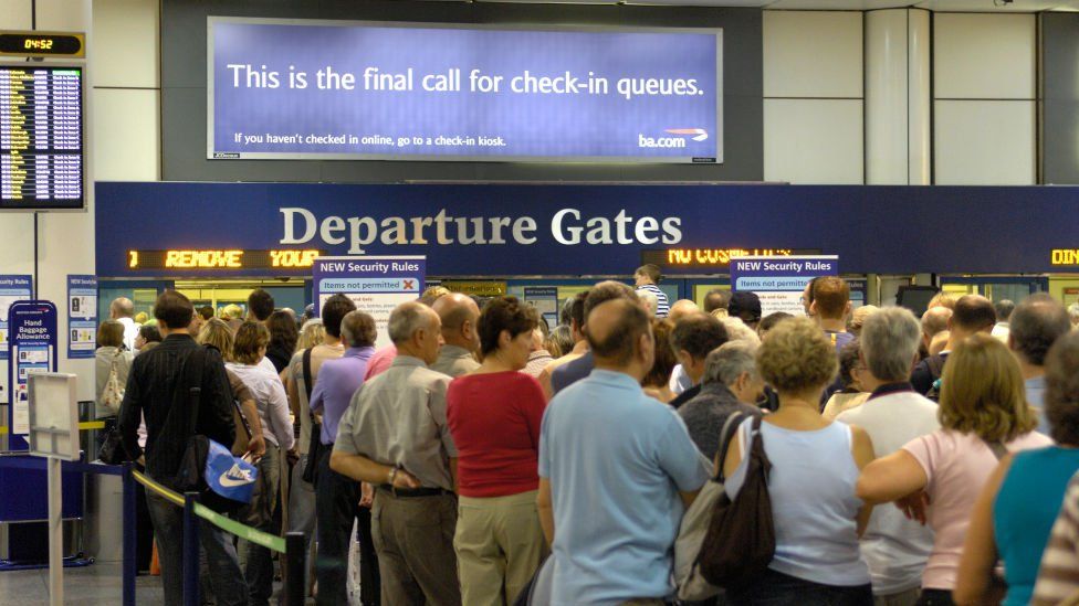 Passengers standing by an airport departure gate sign