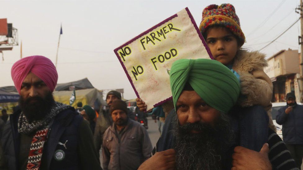 A child on a adult's shoulders holding a sign saying 'no farmer no food'