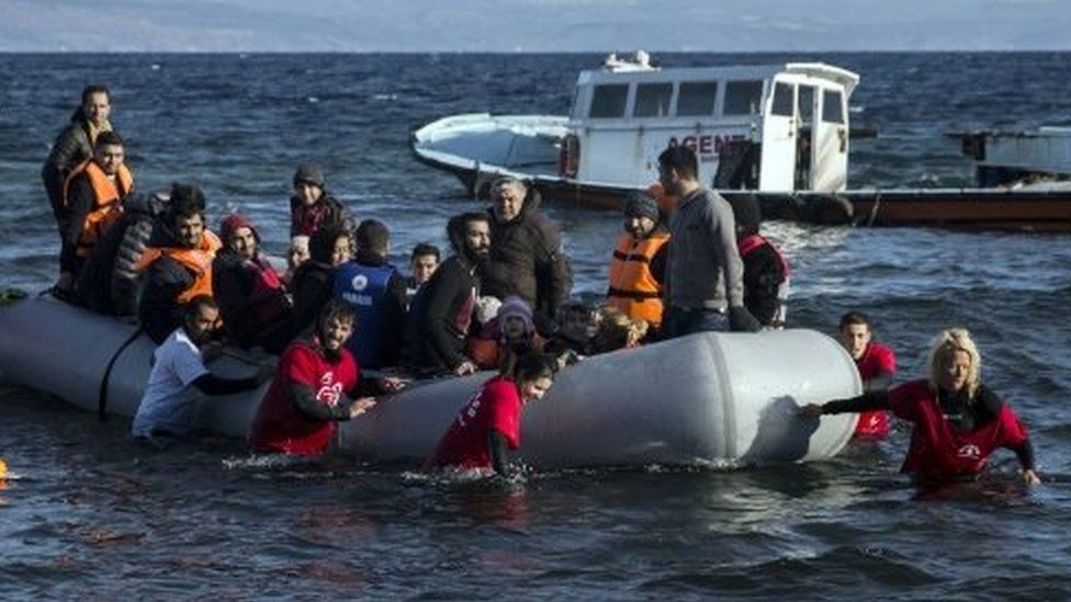 Volunteers help refugees and migrants to disembark from a dinghy after their arrival from the Turkish coast to the Greek island of Lesbos (30 November 2015)