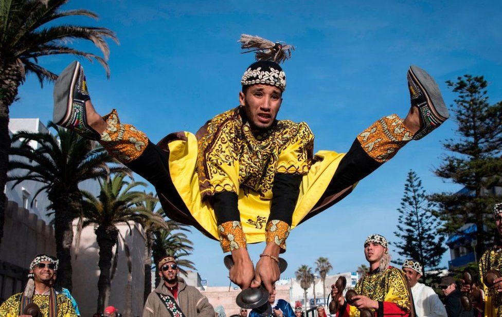 A man jumps in the air as he plays steel hand-held cymbals, called krakebs.