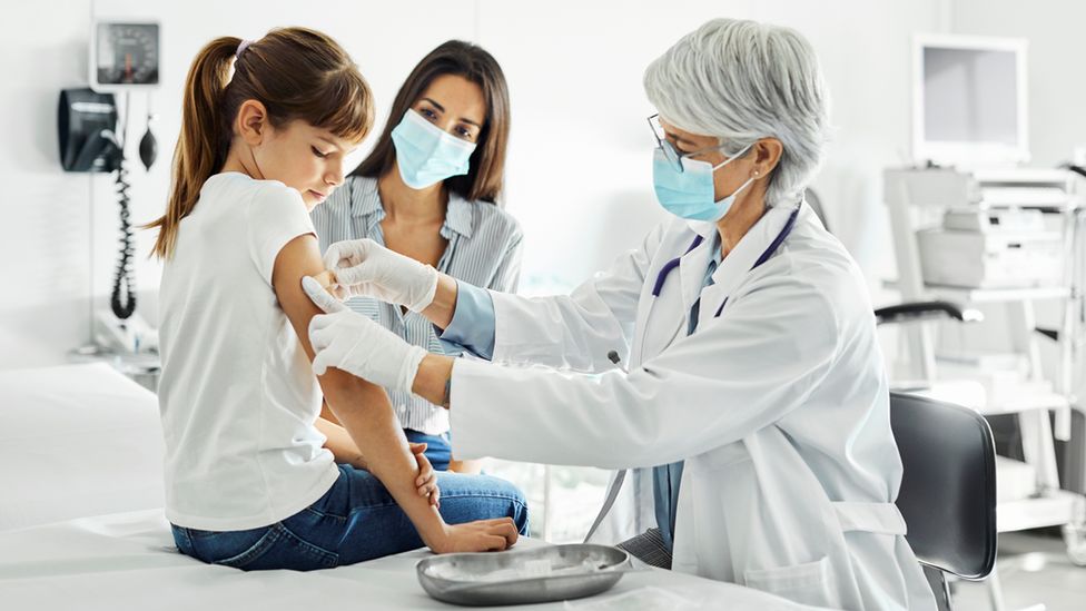 Child being given a vaccine by a doctor while her mother watches