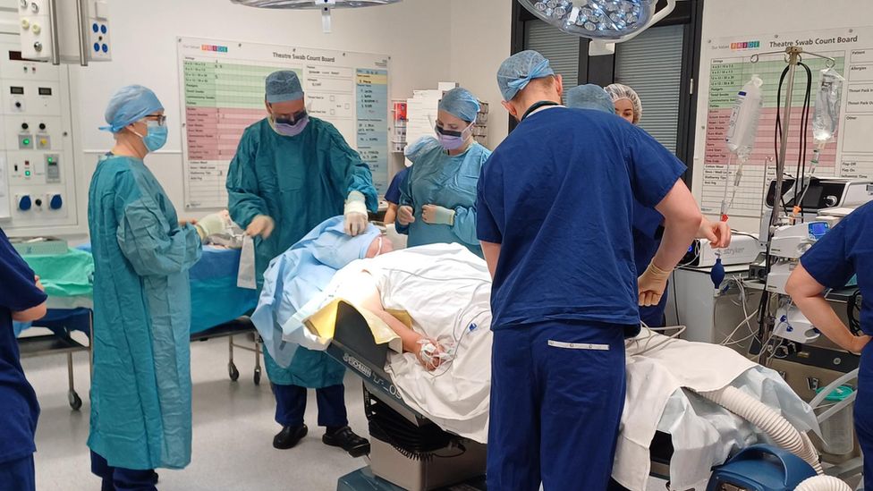 A patient is surrounded by a surgical team in an operating theatre, before surgery