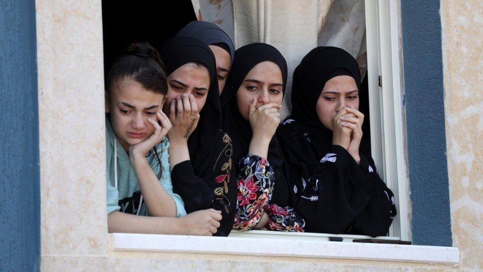 Palestinian relatives watch as mourners carry the body of Yaseen Hamad during his funeral in the West Bank on 16 May