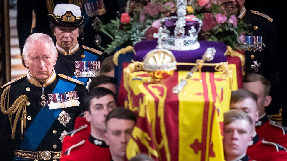 The coffin of Queen Elizabeth II, draped in the Royal Standard with the Imperial State Crown and the Sovereign's Orb and Sceptre, is carried by the bearer party