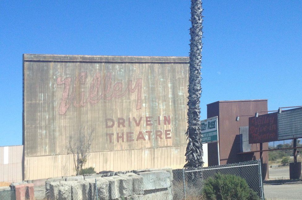 Remnants of an old movie theatre lie on a concrete wall which reads "Valley drive in theatre"."