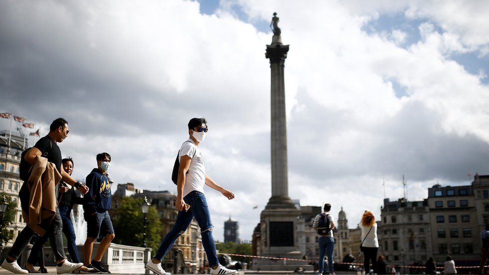 People wearing protective face masks walks through Trafalgar Square, amid the coronavirus (COVID-19) outbreak, in London