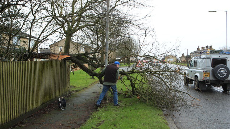 A man works to remove a tree blown over by Storm Dennis in Birkenshaw on the outskirts of Bradford