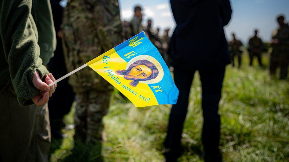 Una bandera religiosa con los colores ucranianos es sostenida durante una sesión informativa sobre el terreno mientras los capellanes militares ucranianos completan su formación