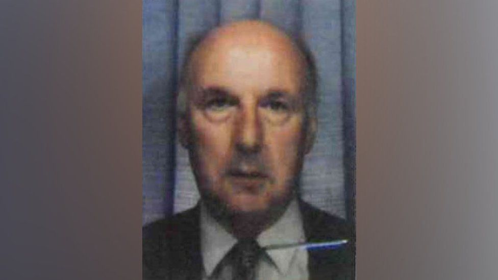 Photo of Ronald Gale from his bus pass. Shows an older man wearing a dark suit jacket and tie over a white shirt. He has a partially bald head.