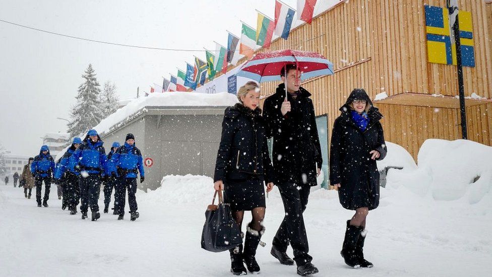 People walk through the resort town of Davos as snow falls ahead of the World Economic Forum (WEF) 2018 annual meeting, on January 22, 2018 in Davos