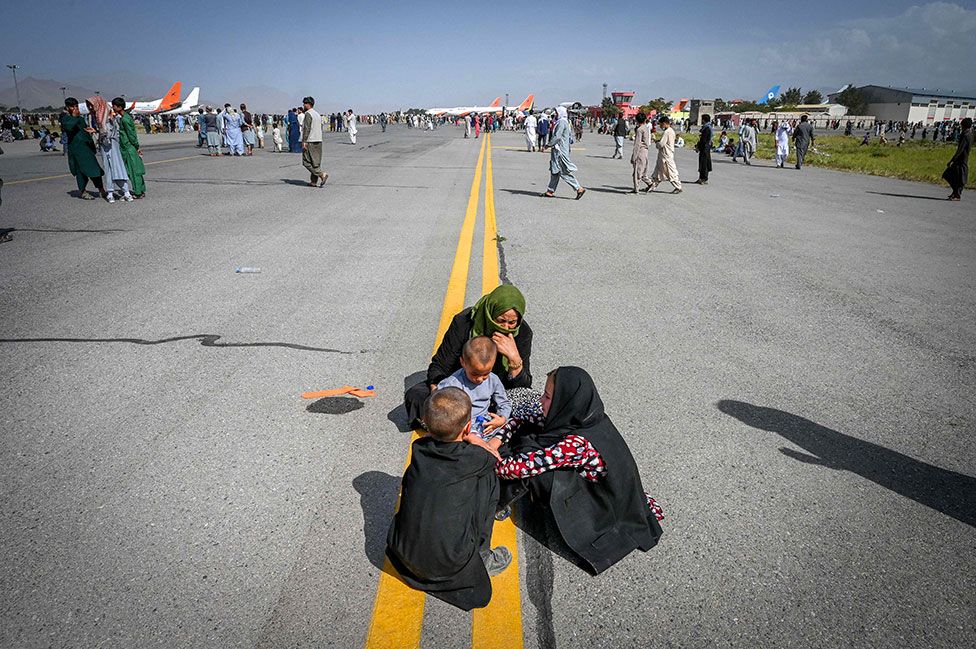 Афганцы сидят на взлетной полосе, ожидая выхода из аэропорта Кабула в Кабуле 16 августа 2021 г.