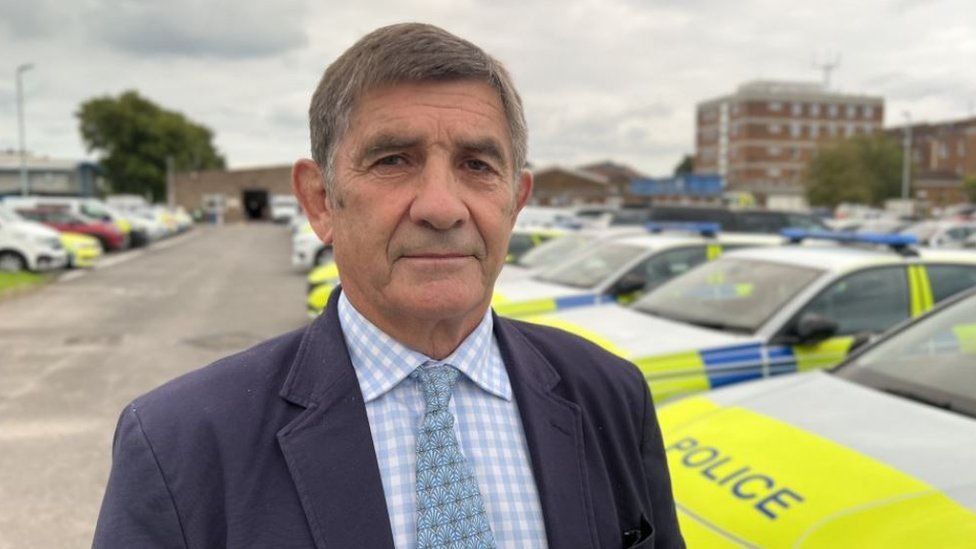 Wiltshire's Police and Crime Commissioner Philip Wilkinson standing in front of a line of police cars.
