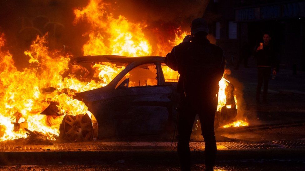 Men take pictures of a burning car during violent protests in Santiago