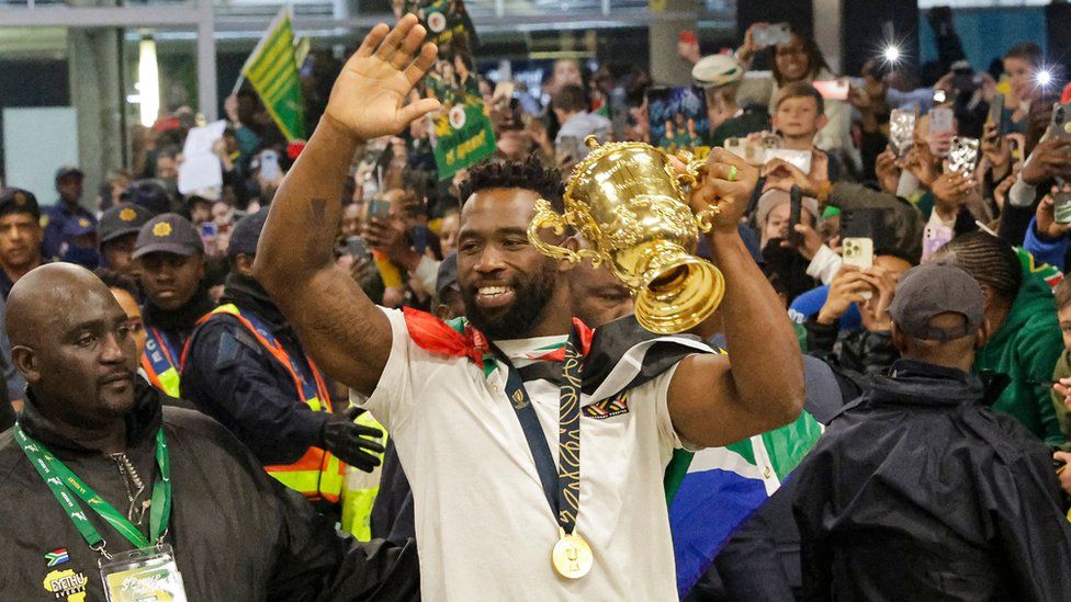 Captain Siya Kolisi greets supporters as he holds the Webb Ellis Cup upon the South African rugby team's arrival