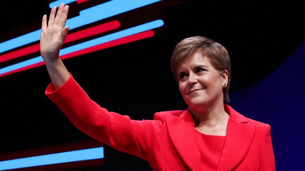 Nicola Sturgeon waves to a assemblage  from the stage, dressed successful  a trademark reddish  suit