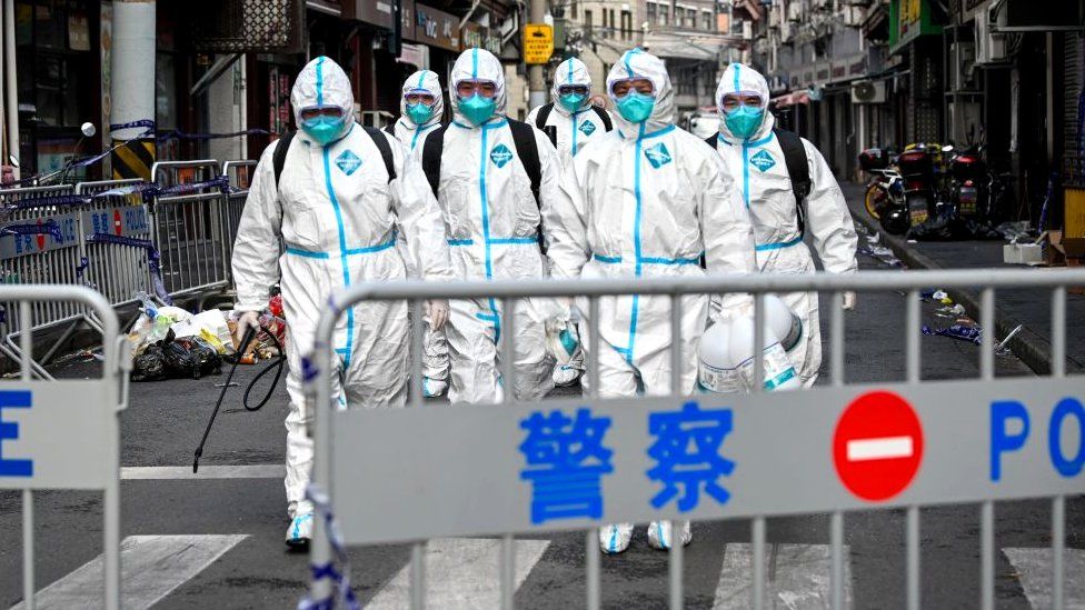 Health workers in protective gear walk out from a blocked off area after spraying disinfectant in Shanghai's Huangpu district