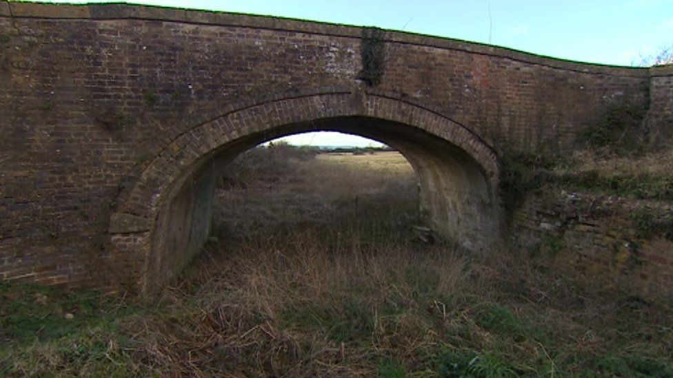 Image shows the "missing mile" section of the Stroudwater canal overgrown and under a bridge