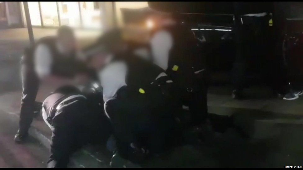 Still from mobile phone footage showing police officers restraining someone during arrest,