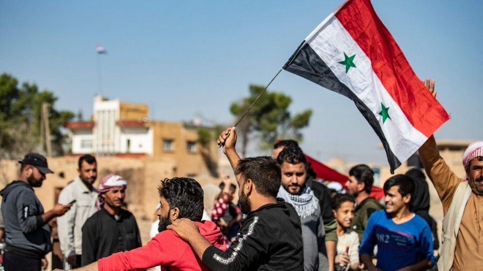 Locals welcome Syrian regime forces as they arrive at the western entrance of the town of Tal Tamer