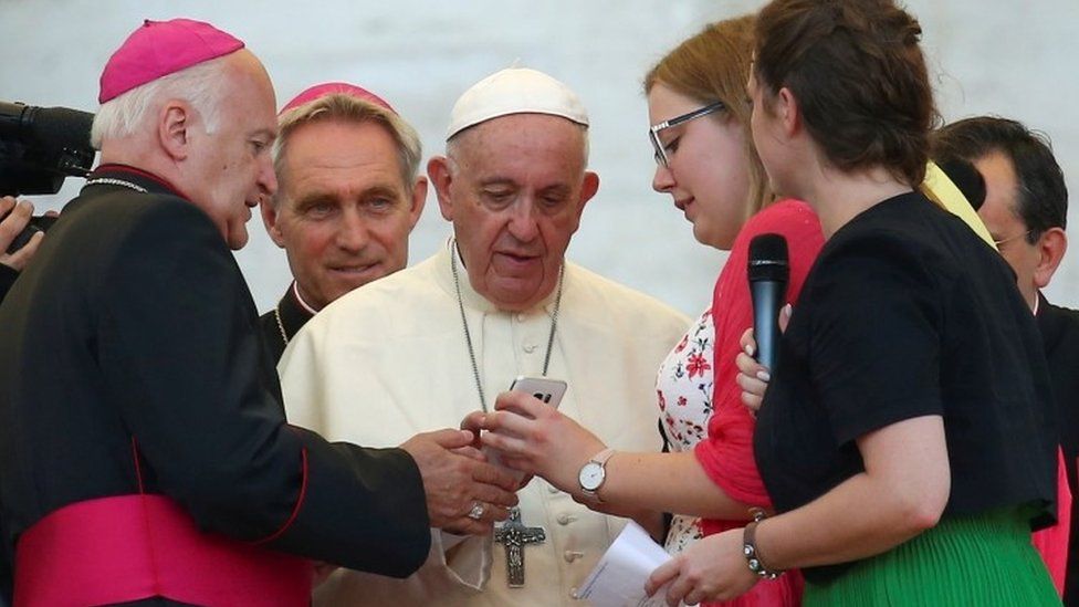 A priest shows Pope Francis a phone