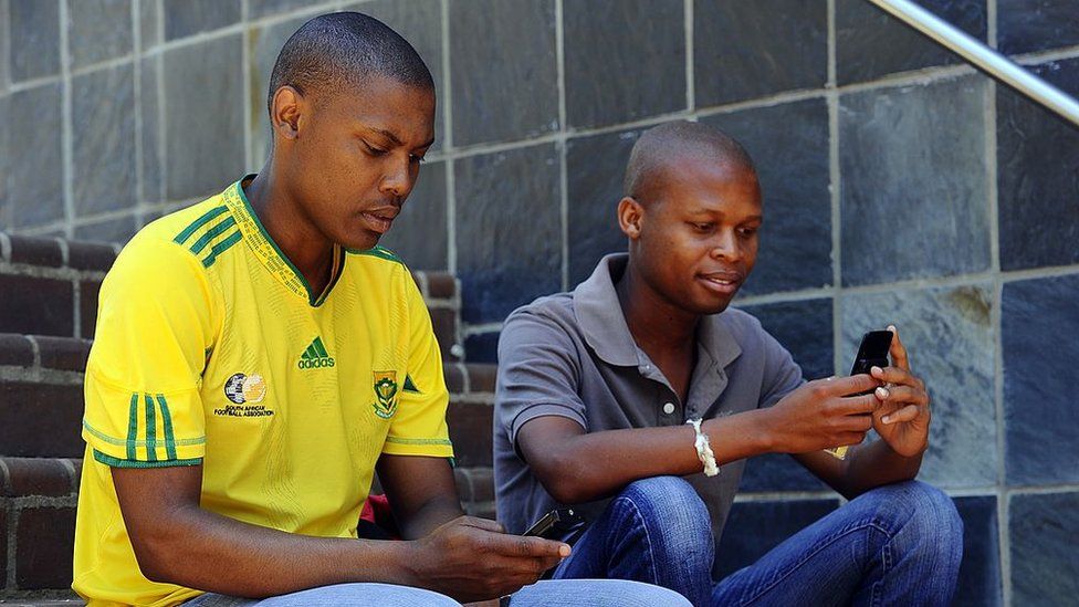 two south african men sitting on the steps using their mobile phones