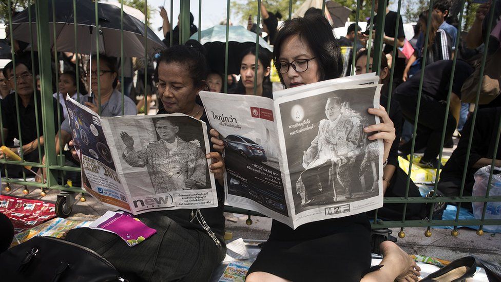 Thai women read newspapers covering the death of King Bhumibol Adulyadej