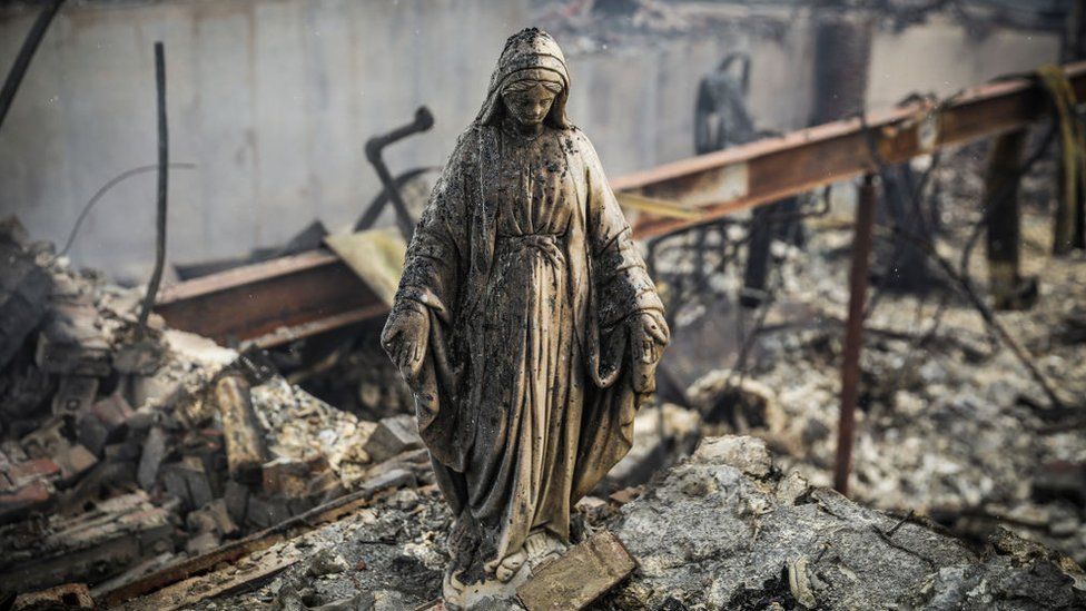 A statue of the Virgin Mary among remains of houses