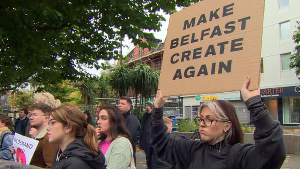 A woman holds up sign that reads: MAKE BELFAST CREATE AGAIN