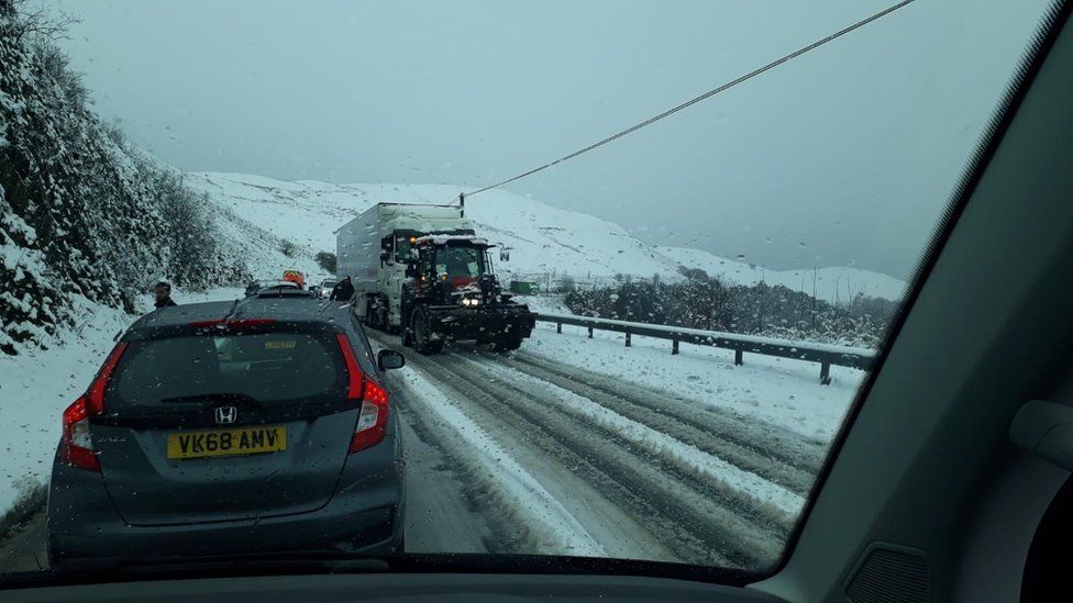 A tractor pulling a lorry up a hill in the snow