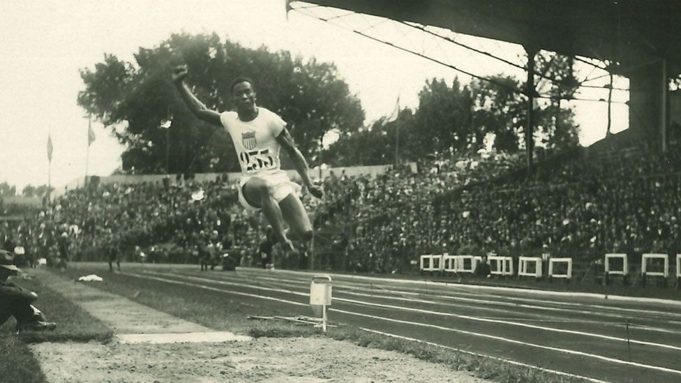 A close-up of a black and white postcard showing William DeHart Hubbard in mid-air doing a long jump in 1924