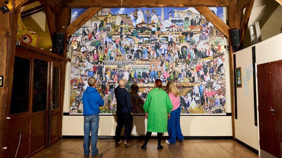 The mural at a distance in the barn with four people looking at it